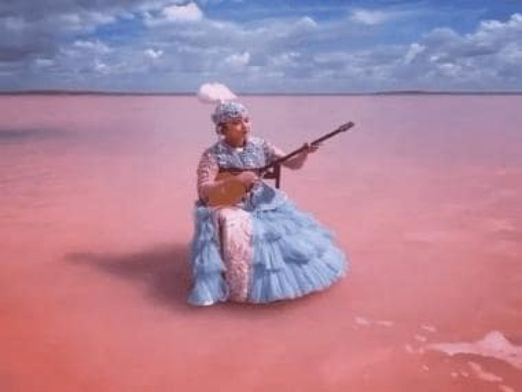 With pink-coloured lake in backdrop, Kazakh woman plays dombyra at Lake Kobeytuz